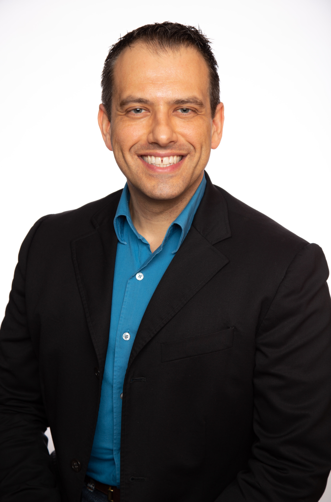 Marat Oyvetsky, PMP, CISSP, the latest Distinguished Cheetah Alum recognized for Inspiring Others. Seated in a black suit jacket with blue shirt, smiling.