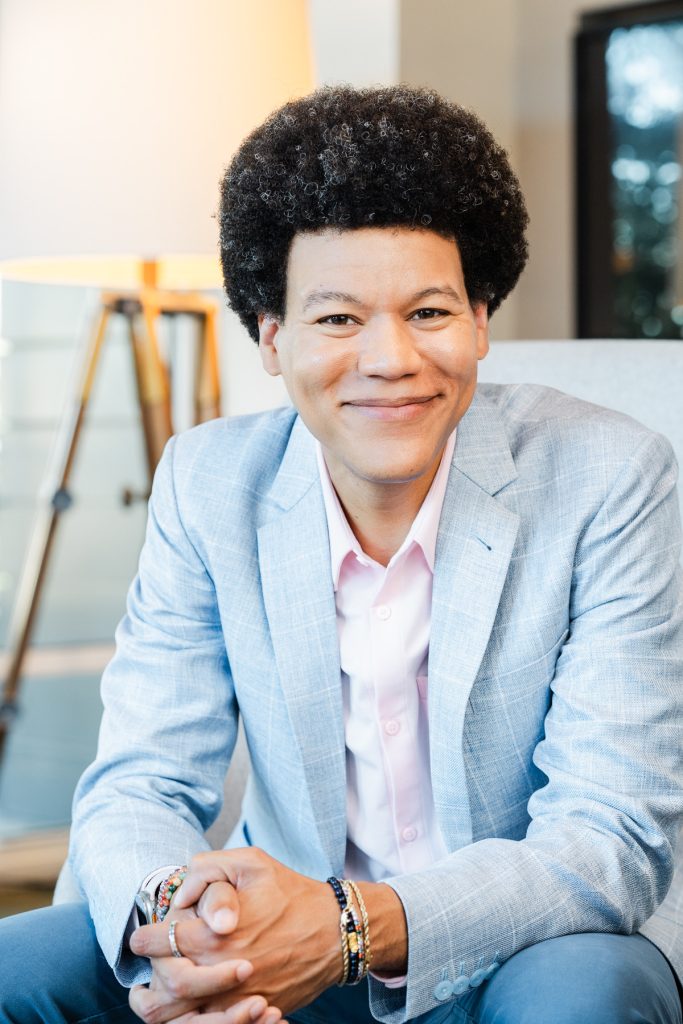 Bernard Usher, PMP, sitting for a professional picture. He has black hair and is wearing a light blue suit jacket. He is smiling.
